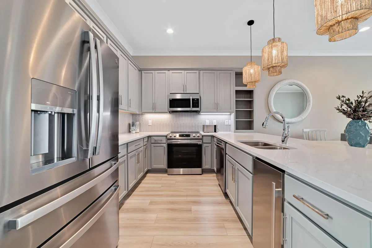 A modern, spotless kitchen featuring stainless steel appliances, a pristine kitchen island with an integrated sink, and gleaming countertops. The space is well-lit with pendant lights, conveying a sense of fresh cleanliness and order.