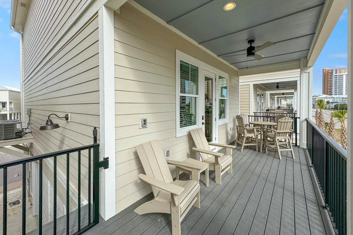 A peaceful outdoor balcony with Adirondack chairs and an outdoor dining table, surrounded by balcony railings and ceiling fans. The view hints at the nearby coastline, inviting guests to unwind, dine, and enjoy partial Gulf Coast sunsets in the fresh sea air.